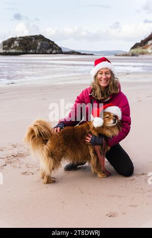 Frau und Hund tragen Santa-Hüte am Strand Stockfoto