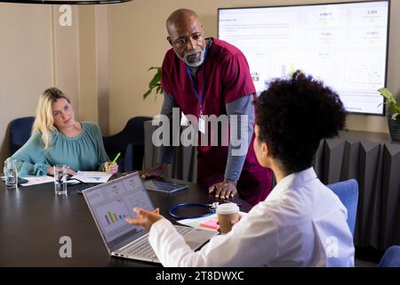 Konzentrierter männlicher Arzt und verschiedene Kollegen sprechen bei Präsentationsbesprechung im Büro Stockfoto