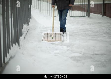 Schneeräumung auf der Straße. Schaufel zur Reinigung der Raupenketten. Der Mann reinigt den Hof. Stockfoto