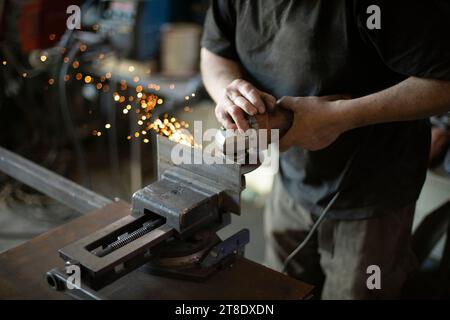 Der Kerl in der Garage repariert Stahlteile. Mann schleift Eisen. Stockfoto