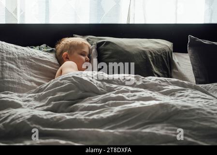 Großer Blick auf einen kleinen Jungen, der friedlich ein Nickerchen auf einem großen Bett mit n macht Stockfoto