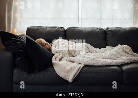 Seitenansicht eines kleinen Jungen, der auf neutralgrauer Couch mit weiß liegt Stockfoto