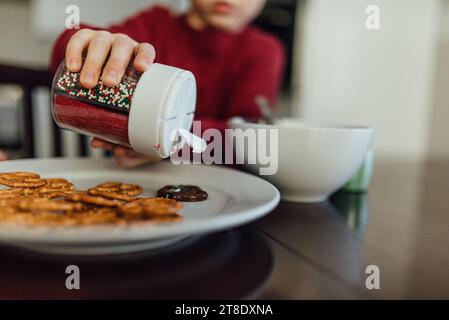 Nahaufnahme eines Kindes, das Brezeln mit weihnachtsstreuseln dekoriert. Stockfoto