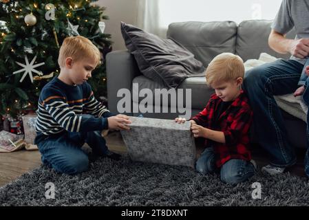 Zwei Jungs sitzen auf dem Boden im Wohnzimmer vor dem weihnachtsbaum Stockfoto
