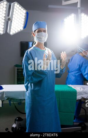 Porträt einer kaukasischen Ärztin mit Gesichtsmaske und Schutzhandschuhen im Krankenhausoperationssaal Stockfoto