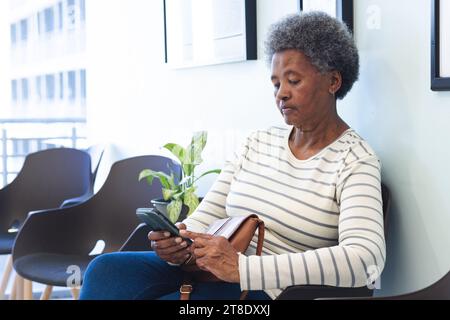afroamerikanische Seniorin mit Smartphone im Wartezimmer des Krankenhauses Stockfoto