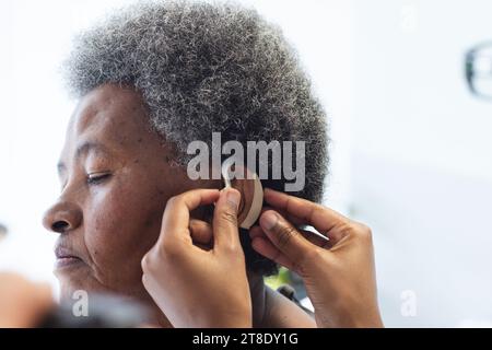 Hände einer afroamerikanischen Ärztin, die Hörgeräte bei Seniorinnen im Krankenhauszimmer anwendet Stockfoto