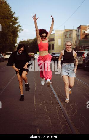 Drei glückliche Freundinnen rennen die Straße runter und springen hoch. Stockfoto