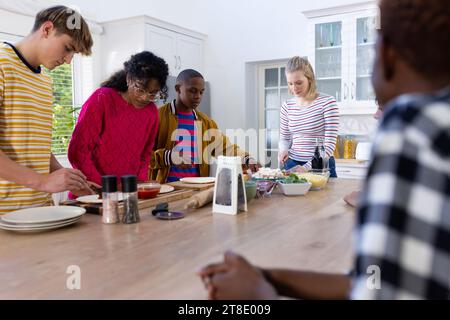 Glückliche, vielfältige Gruppe von Teenager-Freunden, die in der Küche kochen und Pizza machen Stockfoto