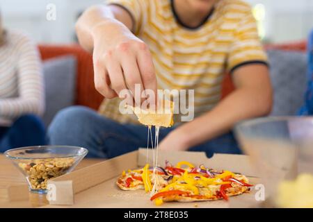 Verschiedene Teenagerfreunde sitzen auf der Couch und essen Pizza Stockfoto