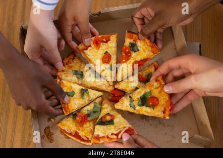 Verschiedene Teenager-Freunde teilen sich Pizza auf dem Tisch zu Hause Stockfoto
