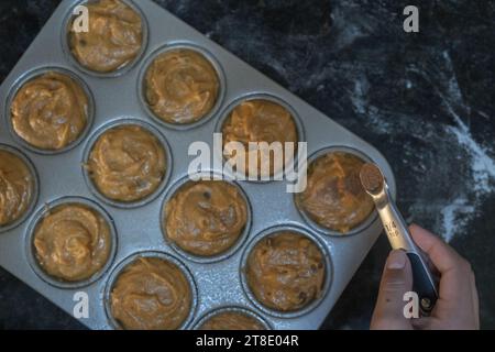 Mit einer Hand, die ungebackene Muffins mit Gewürzen belegt. Stockfoto