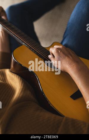 Senior Biracial Mann sitzt auf der Couch und spielt Gitarre zu Hause Stockfoto