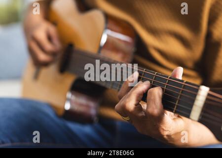 Senior Biracial Mann sitzt auf der Couch und spielt Gitarre zu Hause Stockfoto