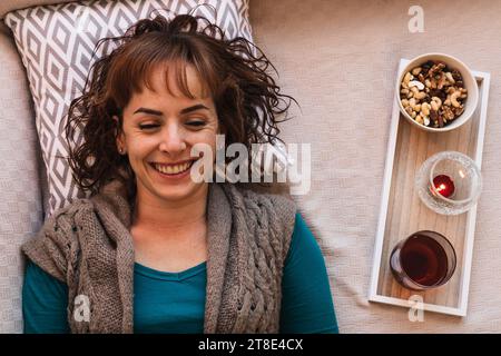 Horizontale, hübsche mitteljunge Frau, kaukasisch, mit kurzen Haaren, lässig gekleidet, lachend mit einem Aufguss und ein paar Nüssen an ihrer Seite. Stockfoto