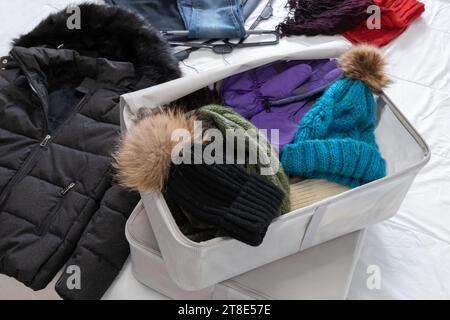 Horizontales Foto, Winterkleidung auf einem Bett, Wollhüte und Schal, versteckt in Stoffkisten, die bis Anfang des Frühlings gesammelt werden sollen. Wandwechsel. Stockfoto