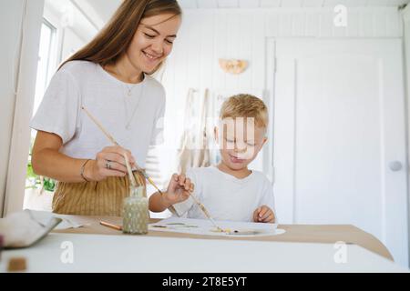 Mom zeichnet mit ihrem Sohn, Junge versucht es, er streckt seine Zunge raus Stockfoto