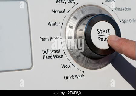 Ein Finger, der die Taste Start PLODE an einer Waschmaschine drückt Stockfoto