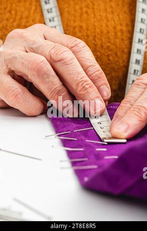 Extremes vertikales Nahfoto, Hände von Reifen erwachsenen Frauen, Kaukasierin, Näherin, Schneiderarbeit, Messen und Markieren mit Stiften. Stockfoto