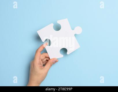 Eine weibliche Hand hält ein weißes Puzzleteil auf blauem Hintergrund Stockfoto