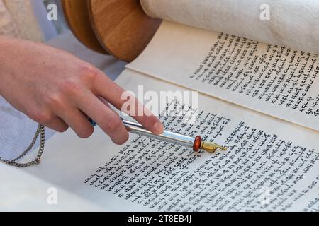 Nahaufnahme einer Hand, die einen yad oder Zeiger hält, um den Leser durch den hebräischen Text der jüdischen Thora zu führen. Stockfoto