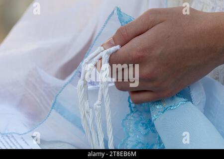 Nahaufnahme eines jüdischen Mannes, der betet, während er die Fäden oder Zit-Zit auf seinem Tallit in der Hand hält und das Schema jisrael rezitiert. Stockfoto