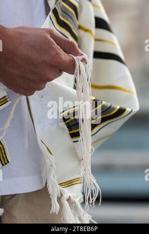 Nahaufnahme eines jüdischen Mannes, der betet, während er die Saiten oder Zitzit auf seinem Tallit in der Hand hält und das Schema jisrael rezitiert. Stockfoto