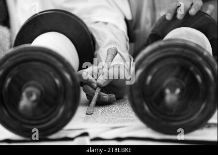 Detaillierte Nahaufnahme der Hand eines Mannes Halten Sie ein yad oder einen Zeiger, während Sie aus einer Schriftrolle der Thora oder fünf Bücher von Moses lesen. Stockfoto