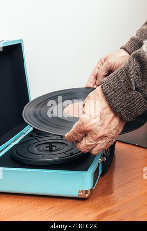 Vertikales Nahaufnahme-Foto, männlicher älterer Erwachsener, Kaukasier, Rücken gedreht, in braunem Wollpullover gekleidet. Platzieren einer Musikvinyl auf einem Plattenspieler. Stockfoto