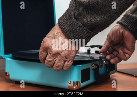 Nahaufnahme horizontales Foto, älterer Erwachsener männlich, Kaukasier, Rücken gedreht, in braunem Wollpullover gekleidet. Platzieren einer Musikvinyl auf einem Plattenspieler. Stockfoto