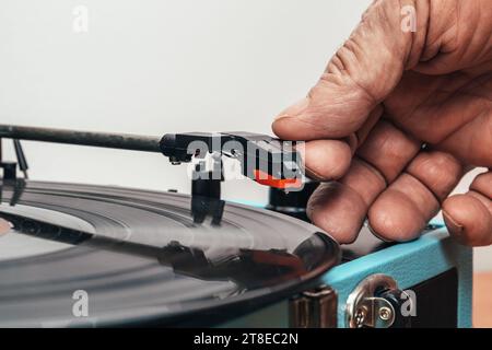 Extrem Nahaufnahme horizontales Foto, Hand eines älteren männlichen Erwachsenen, Kaukasier, auf Vinyl platziert, Kopf eines Plattenspielers in Form eines blauen Koffers. Stockfoto