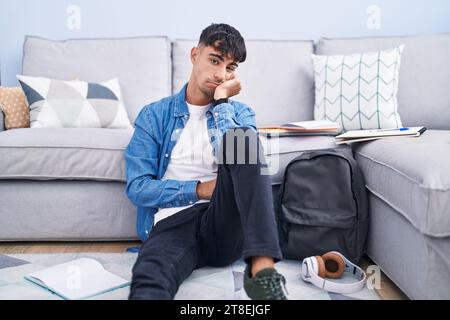 Junger hispanischer Mann, der auf dem Boden sitzt und für die Universität studiert, denkt müde und gelangweilt aus mit Depressionen, Problemen mit gekreuzten Armen. Stockfoto