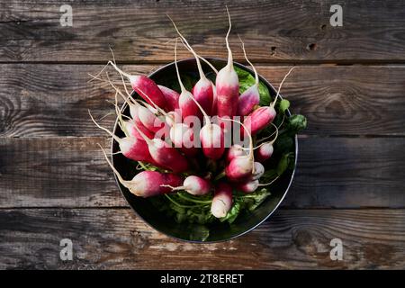 Ein Haufen frischer, ganzer Radieschen in einer Schüssel auf einem alten Holztisch, von oben gesehen, herbstliche Atmosphäre. Stockfoto