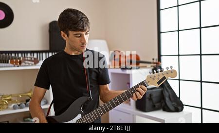 Attraktiver junger hispanischer Mann, der intensiv elektrische Gitarre im Musikstudio spielt, ein Porträt eines erwachsenen Musikers, der sich auf sein Instrument, Creatin, konzentriert Stockfoto