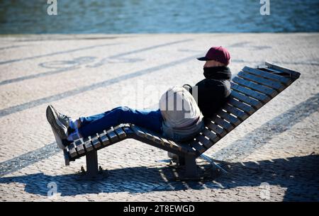 Obdachloser, der im Winter auf einer Bank am Fluss sitzt. Stockfoto