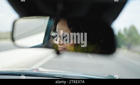 Eine hispanische Frau mittleren Alters, die Auto fährt und auf der Straße in den Rückspiegel schaut Stockfoto