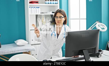 Eine junge, wunderschöne hispanische Ärztin, die sich Röntgenbilder mit einem Computer ansieht, der in der Klinik steht Stockfoto