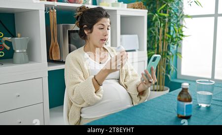 Junge schwangere Frau, die eine Online-medizinische Beratung hält Pillen im Speisesaal Stockfoto