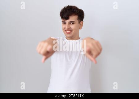 Junger nicht binärer Mann, der ein lässiges weißes T-Shirt trägt, das mit den Fingern auf dich und die Kamera zeigt, positiv und fröhlich lächelnd Stockfoto