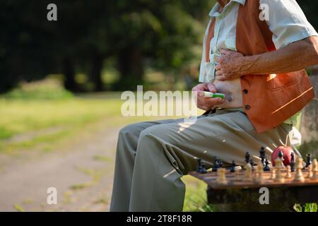 Älterer Diabetiker, der Insulin in den Abdomen injiziert. Nahaufnahme eines älteren Mannes mit Typ-1-Diabetes, der im Stadtpark mit Spritzennadel isoliert. Stockfoto