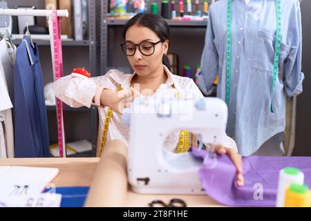 Junge arabische Schneiderin, die in einem Atelier arbeitet und die Zeit auf der Armbanduhr überprüft, entspannt und selbstbewusst Stockfoto