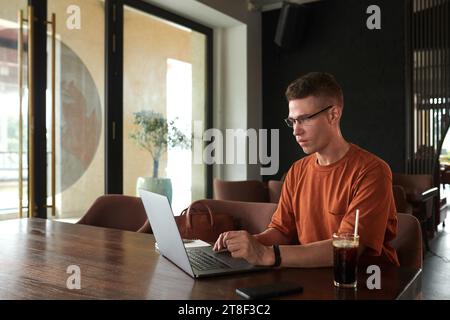 Ernster junger Mann in Brille, der am Kaffeetisch sitzt und am Laptop arbeitet Stockfoto