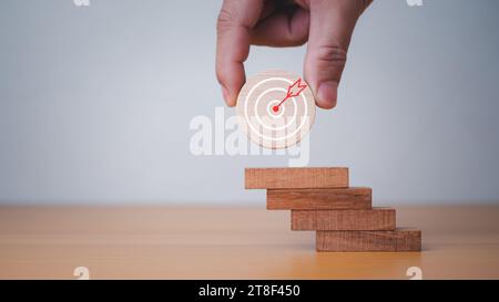 Die Hände des Geschäftsmannes halten ein kreisförmiges Holzbrett mit einer Dartscheibe. Sie stellt das Konzept der Geschäftsstrategie und des Zielaktionsplans dar. Stockfoto