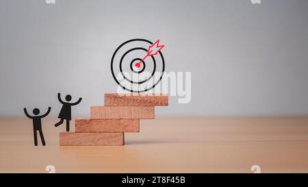 Mitarbeiter der Firma klettern die quadratischen Holzstufen hinauf, um zum Dartbrett zu gelangen. Sie stellt das Konzept der Geschäftsstrategie und des Zielaktionsplans dar. Stockfoto