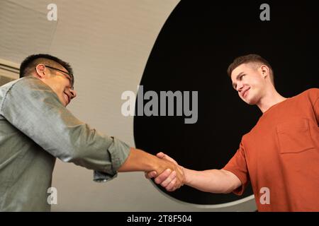 Fröhlicher junger Geschäftsmann begrüßt den Projektgründer und schüttelt die Hand Stockfoto