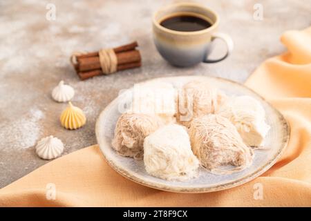Traditionelle arabische Süßigkeiten pishmanie und eine Tasse Kaffee auf braunem Betonhintergrund und orangefarbenem Leinentuch. Seitenansicht, Nahaufnahme, selektiver Fokus. Stockfoto