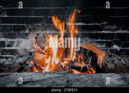 Brennendes Brennholz in der Feuerstelle des Kamins im Landhaus. Rustikaler Backofen mit brennenden Holzstämmen. Stockfoto