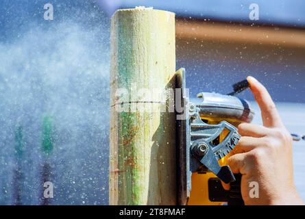 Eine elektrische Säge wird vom Arbeiter verwendet, um Holzpfosten für Zäune zu schneiden Stockfoto