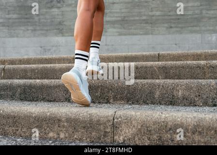 Eine Nahaufnahme der Beine einer lateinamerikanischen Frau, während sie in sportlicher Kleidung Betonstufen aufsteigt und sich auf ihre Schuhe konzentriert. Stockfoto