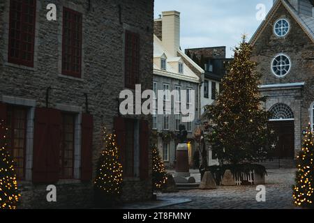 Eine alte kopfsteingepflasterte Straße mit festlichen Weihnachtslichtern, mit einem leuchtenden Baum und rustikalen Steinhäusern unter einem dunklen Himmel in Quebec, Cana Stockfoto